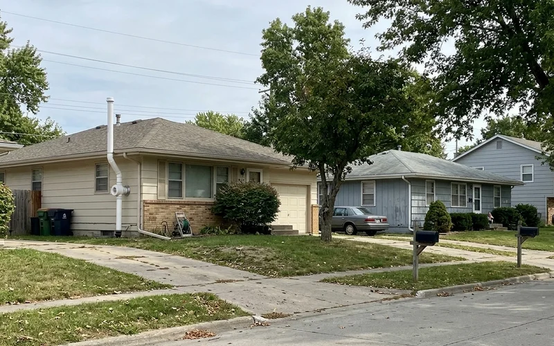 Two neighboring Des Moines houses, one with a radon mitigation pipe
